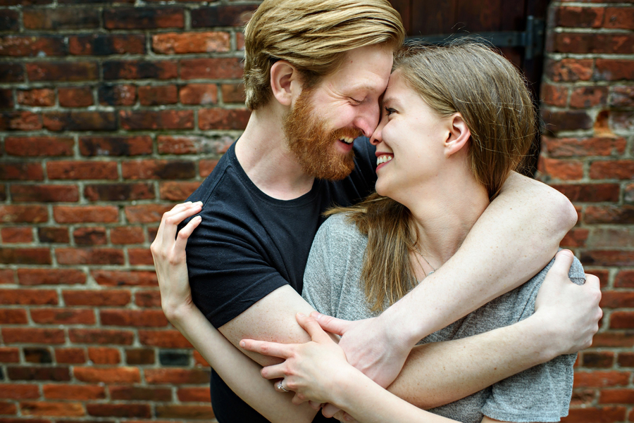 An engaged couple wrap each other up with their arms and smile.